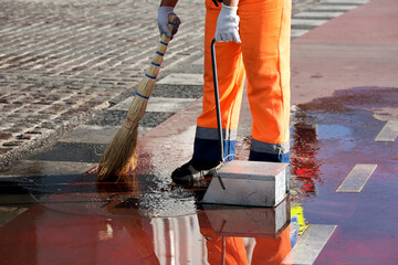 Janitor cleaning wet city road. Legs of street sweeper with broom in a puddle