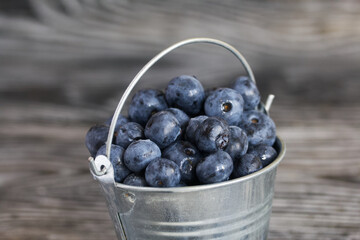 Ripe blueberries in a metal bucket. On pine boards. Close-up.