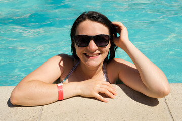 A woman in sunglasses rests in the pool, smiling looking into the camera.