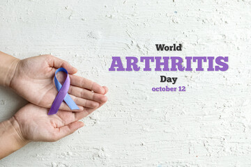 World Autoimmune Arthritis Day. Woman hands holding blue purple ribbon on white background. RA rheumatoid arthritis illness disease.