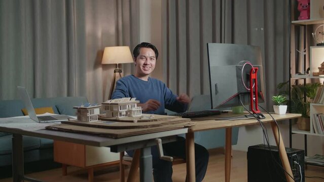 Asian Male Engineer With The House Model Smiling And Crossing His Arms To The Camera While Working On A Desktop At Home
