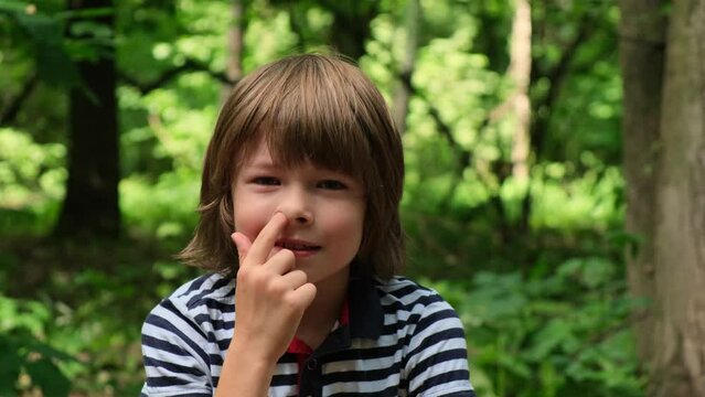 Little boy picks boogers in his nose in park. Slow motion