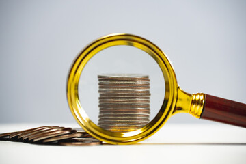 A stack of coins under a magnifying glass. Review of capital and investments. Business model for...