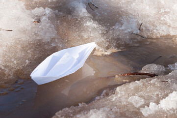 A white paper boat sails along a spring stream among the snowy shores