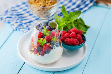 Healthy meal made of granola, yogurt and fruits on painted boards. Diet dessert with yogurt, granola and pomegranate fruit in a glass. Healthy breakfast on a blue surface