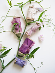 Silky pink, purple, magenta thin ribbons on a wooden roll next to a branch of lathyrus flowers. Festive decor for a wedding and a composition of silk ribbons on a light background