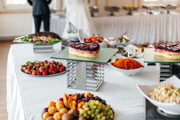  A large buffet table at an event featuring cakes, salads, and fresh fruits.