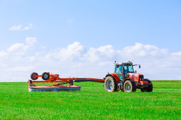 A rotary mower attached to a tractor moves across the field and mows fresh green grass for silage. Preparation of silage for the winter.