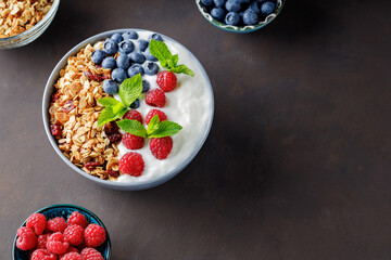Bowl of granola with yogurt and fresh berries on a dark background. Healthy breakfast and various ingredients. Top view. Copy space