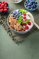 Homemade yogurt bowl with raspberry, blueberry and granola on a green surface. Bowl with yogurt, granola and berries on a green linen napkin. Healthy food concept