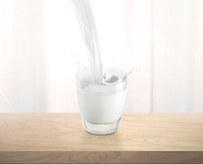 Pouring milk into glass cup with splashing, on wooden table