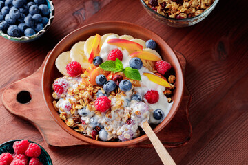 Bowl of homemade granola with yogurt and fresh berries on wooden background. Healthy breakfast with yogurt, granola and fruits on cutting board. Flat lay