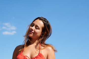 A young woman in summer look enjoying rest with closed eyes in background of blue sky