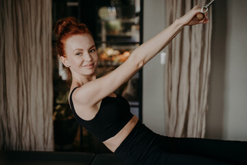 Young ginger female smiling while doing exercises on pilates reformer