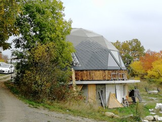 Non traditional spherical dome house constructed from wooden triangles, presenting geodesic architecture, sustainable design approach, and innovative residential building concept. © Semi