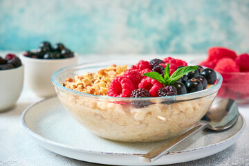 Close-up oatmeal with different berries and crushed nuts in a glass bowl. Healthy balanced food