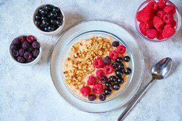 Oatmeal with different berries and crushed nuts in a glass bowl. Healthy balanced food. Top view