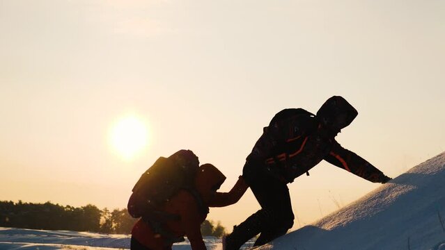 climbers climb snowy mountain sunset winter. teamwork concept. overcoming obstacles together. give helping hand. business teamwork silhouette. hiking path mountains. success active sports backpacks.