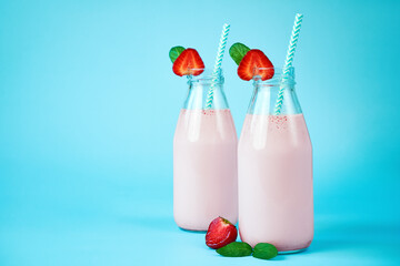 Close-up strawberry smoothie or milkshake in glass jar with berries on blue background.