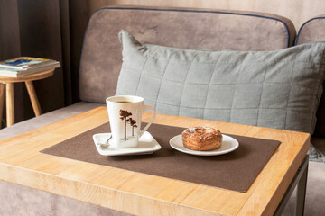 On the coffee table in the living room, a cup of coffee and a cake on a plate.