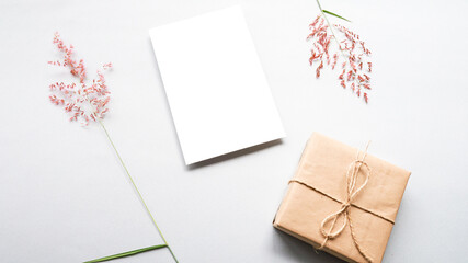 White blank card, gift box and grass flower on gray background