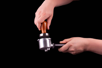 Man is using a tamper to press freshly ground morning coffee into a coffee tablet on isolated black background