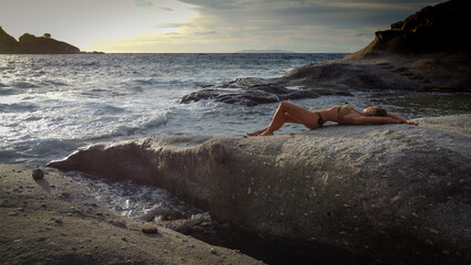 Woman in bikini relaxes on a rock - 523200041