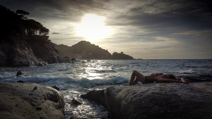 Woman in bikini relaxes on a rock - 523200071