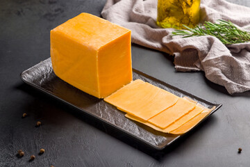 cheddar cheese sliced on black plate on dark table - obrazy, fototapety, plakaty