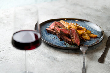 Beef steak sliced with potato wedges and red wine on glass on grey table