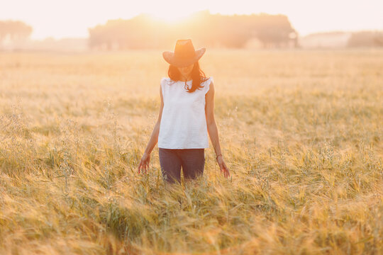 Woman farmer in cowboy hat at agricultural field on sunset.
