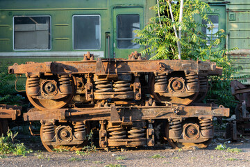 Rusting wagon bogies and old railway equipment from electric locomotives in Tbilisi, Georgia in stock on street on sunny day. Decommissioned soviet engineering put on ground near lush green trees