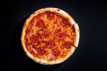 Pizza with tomato sauce, mozzarella, salami, chili, honey on black background. View from above