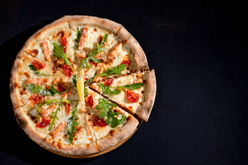 Pizza with salmon, mozzarella, cherry tomatoes, arugula, lemon and parmesan. Italian cuisine. On a black background. Free space for text. View from above.