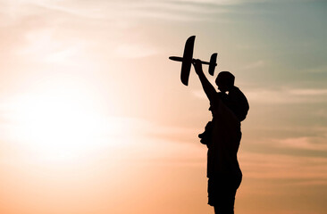 Father and son launch a toy airplane at sunset. Silhouettes of people against the sky. The concept of a friendly family and Father's Day. Air tour. Go on a trip, a flight and a vacation.