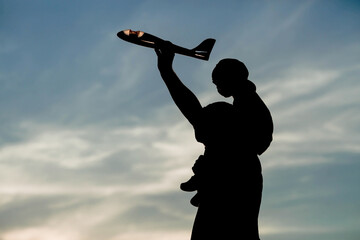 Father and son launch a toy airplane at sunset. Silhouettes of people against the sky. The concept...