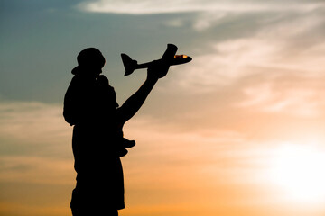 Father and son launch a toy airplane at sunset. Silhouettes of people against the sky. The concept of a friendly family and Father's Day. Air tour. Go on a trip, a flight and a vacation.