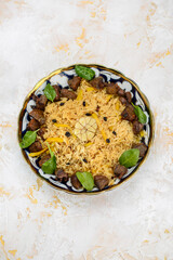 pilaf with meat, raisins and greens in a painted plate on a white background, vertical photo
