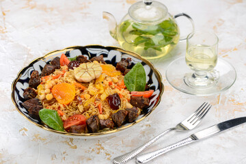 pilaf with meat, plum and apricot in a painted plate on the table with tea
