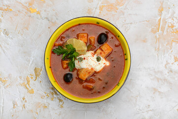 red soup with salmon and olives in a yellow plate
