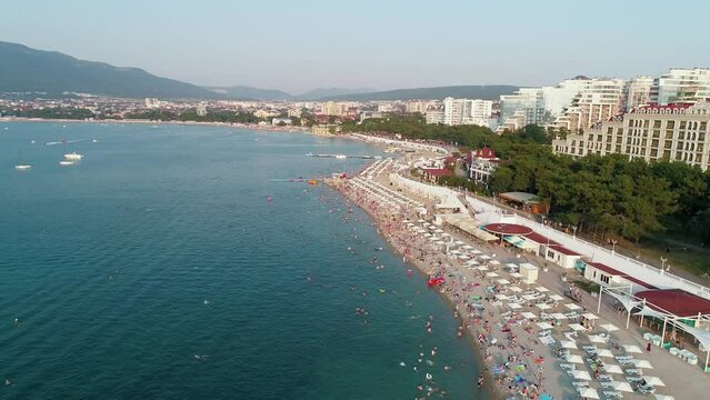 Aerial view of a bay of the resort city of Gelendzhik. Transparent turquoise sea water and the beach with white sunbeds and sun umbrellas on a beautiful summer day