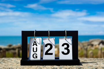 Aug 23 calendar date text on wooden frame with blurred background of ocean.