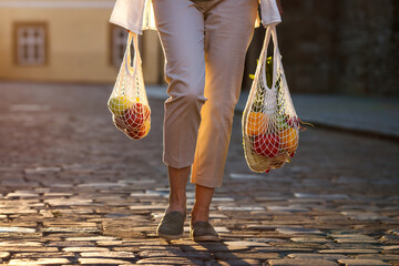 Woman walks on street and carrying reusable mesh bag after shopping