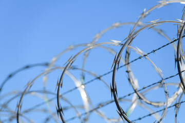 Coils of razor wire on a secuity fence against blue sky with nearest section in focus and defocused...