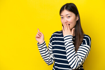 Young Chinese woman isolated on yellow background with surprise expression while pointing side