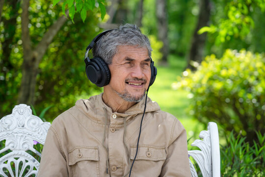 Portrait Happy Senior Man With Grey Hair And Beard Wearing Headphones For Listening Music, An Old Asian Man Relaxing In The Park