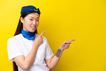 Airplane Chinese woman stewardess isolated on yellow background pointing finger to the side and presenting a product