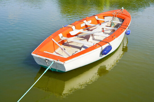White boat with oars on the water. White training wooden boat with red trim sits on a smooth water surface. Smooth water is reflecting the image of the boat