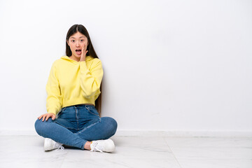 Young Chinese woman sitting on the floor isolated on white wall with surprise and shocked facial expression
