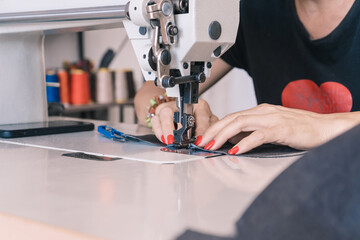 The seamstress sews at the sewing machine, threads the fabric. Women's hands